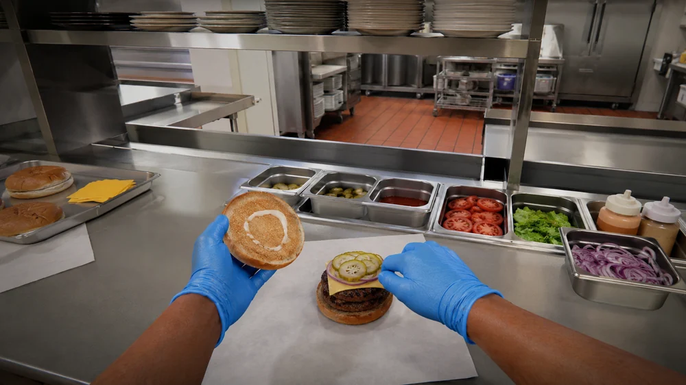 First-person view of gloved hands assembling a burger in VR training